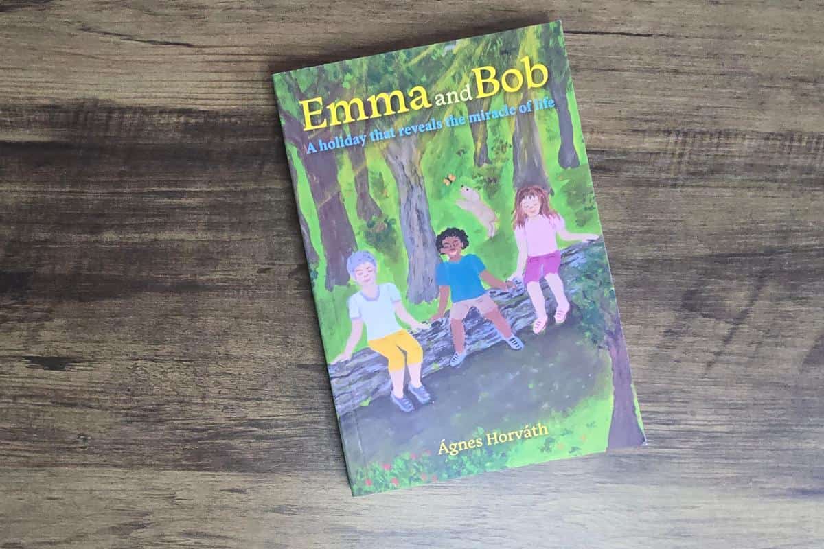 A children's book titled "Emma and Bob" by Ágnes Horváth rests on a wooden surface. This charming book for children showcases an illustrated cover with kids sitting on a log in the heart of a forest.