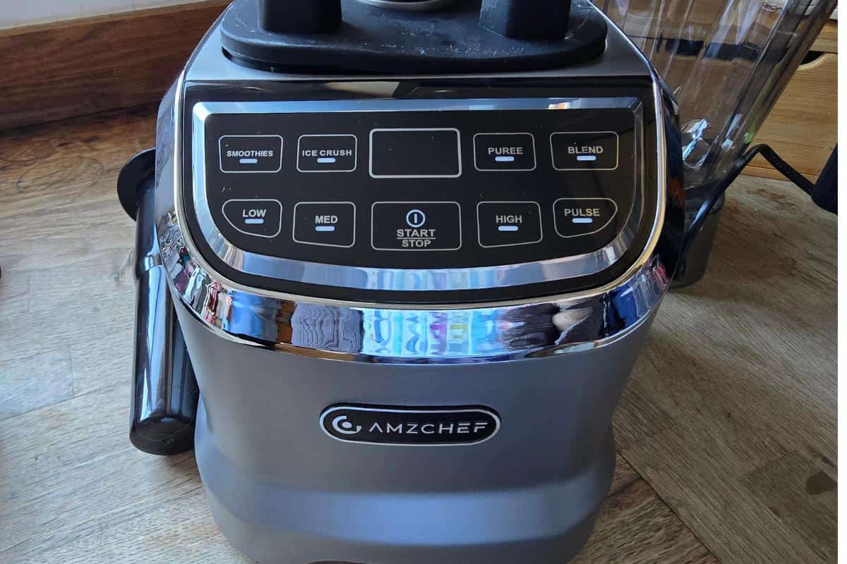 Close-up of the AMZCHEF Blender Model 5003 control panel on a wooden floor, featuring buttons for smoothies, ice crush, puree, high, medium, low, and pulse, with a central start/stop button—perfect for any kitchen.