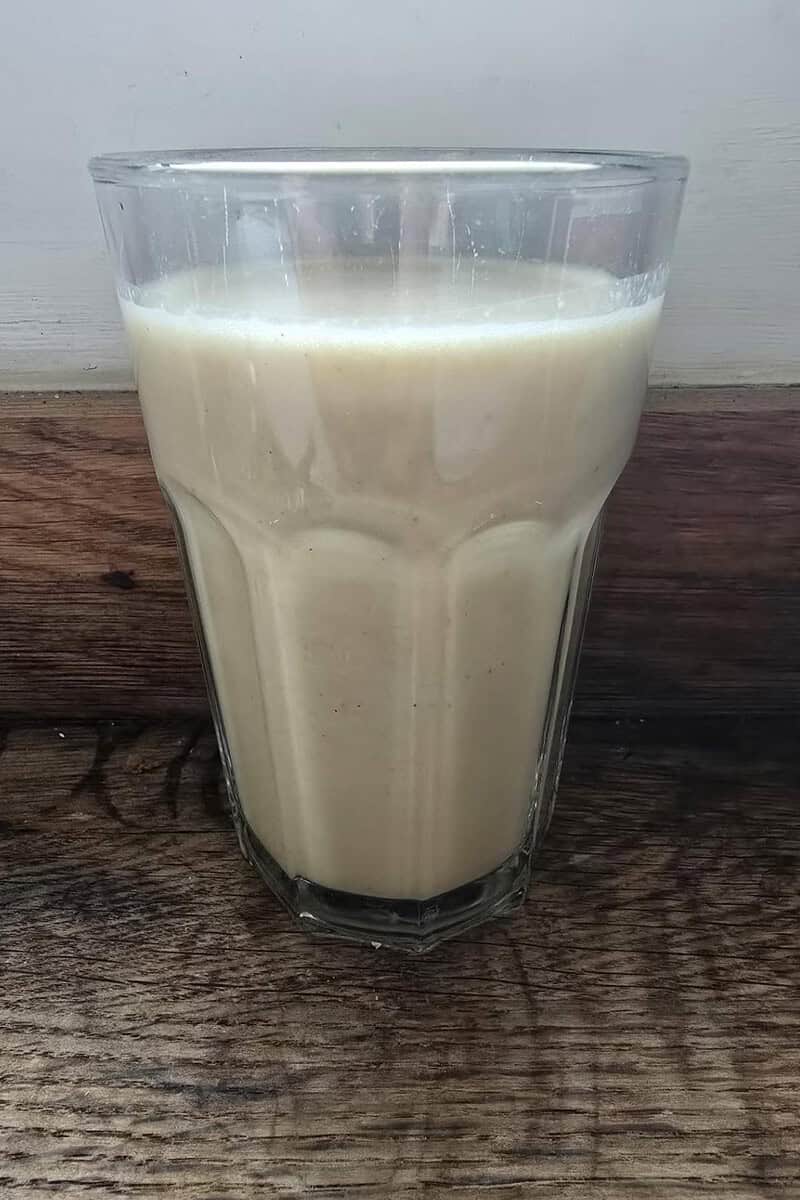 A glass filled with a light brown creamy beverage, skillfully crafted using the AMZCHEF Blender, rests elegantly on a wooden surface.