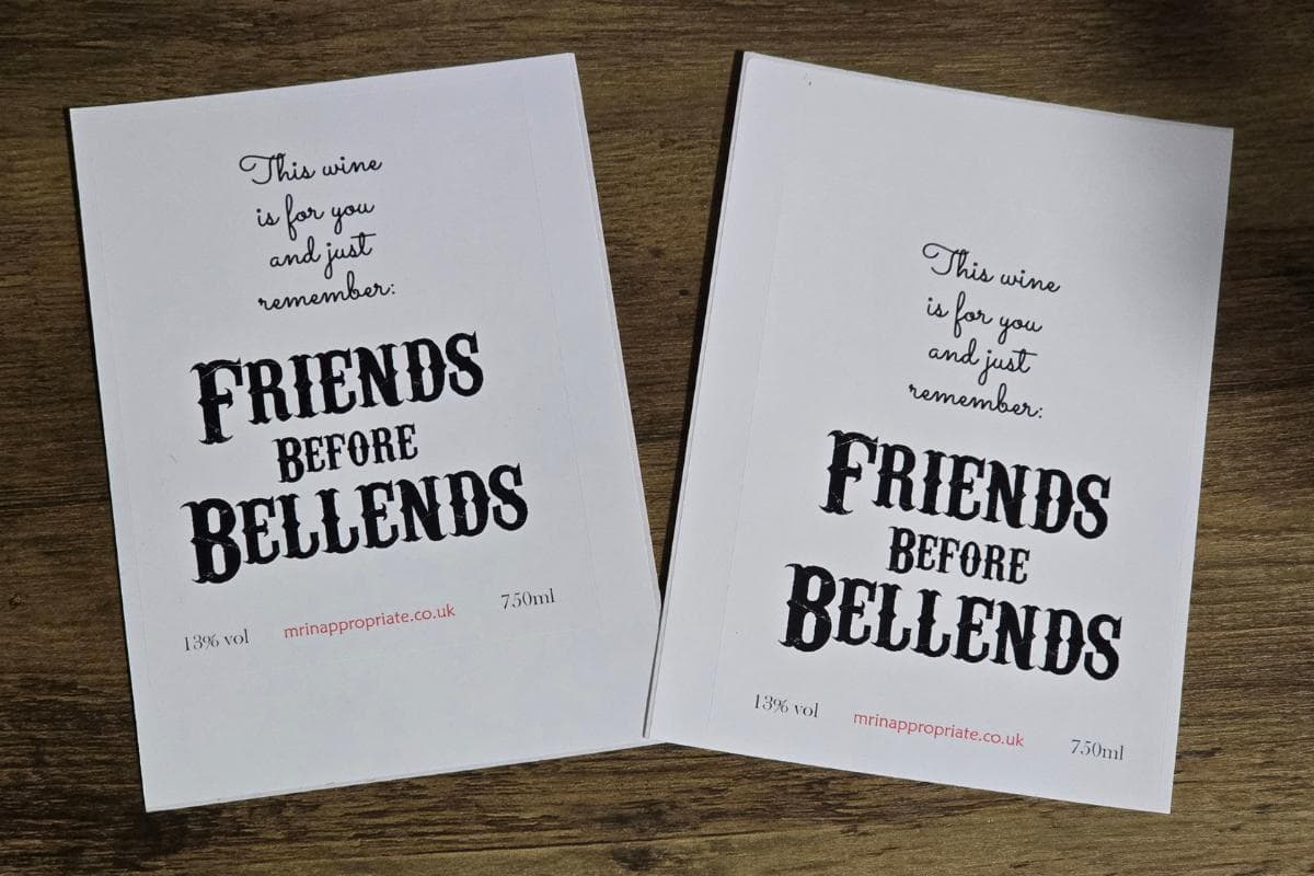 Two white cards on a wooden surface read: "This wine is for you, and just remember: FRIENDS BEFORE BELLENDS." Both cards display wine measurements and a website link. A perfect rude gift that might make them laugh and blush!.