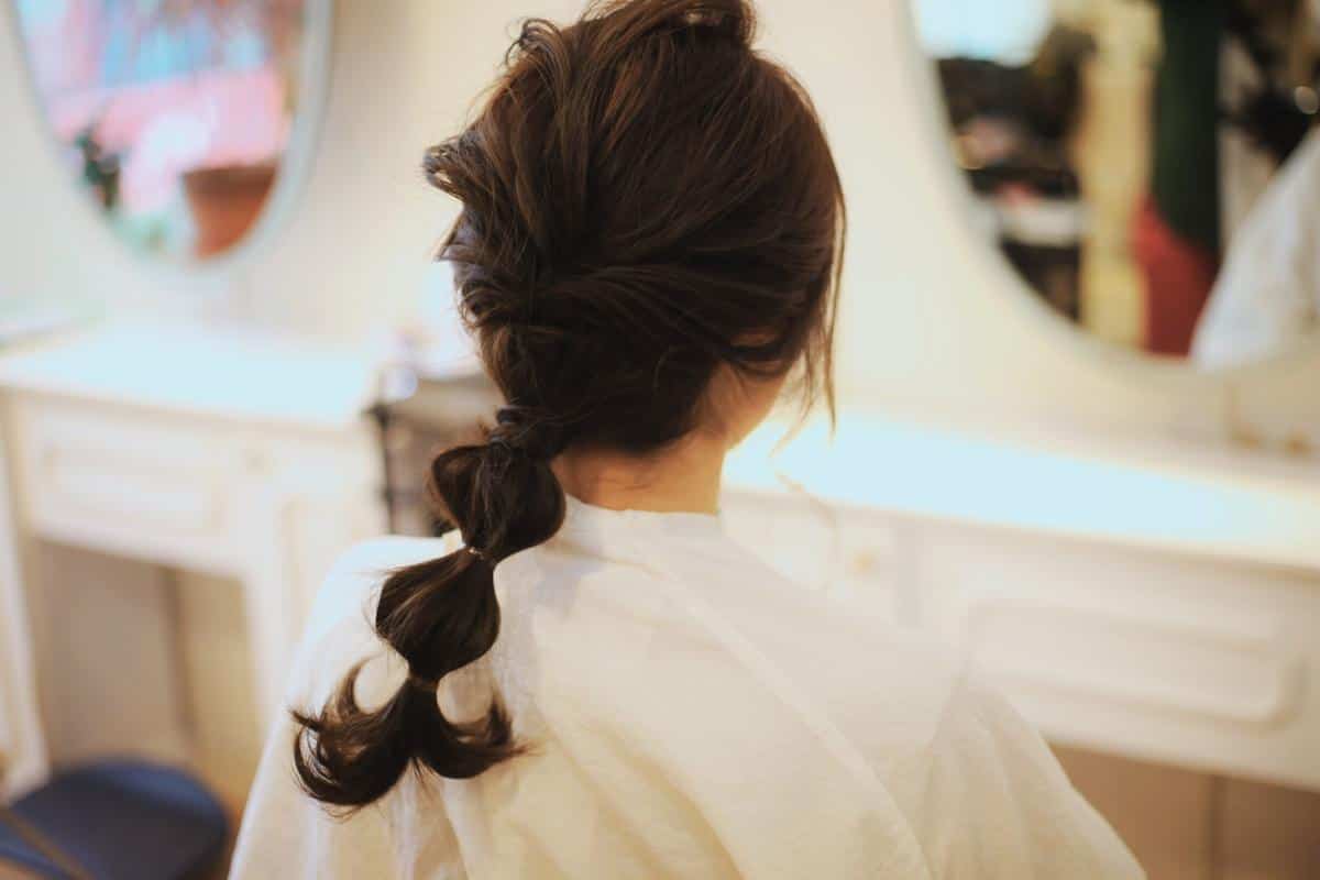 A fitness lover with dark, wavy hair in a styled ponytail sits in front of a vanity mirror in the well-lit room. This effortless hairstyle is perfect for someone always on the move, embracing both style and practicality.