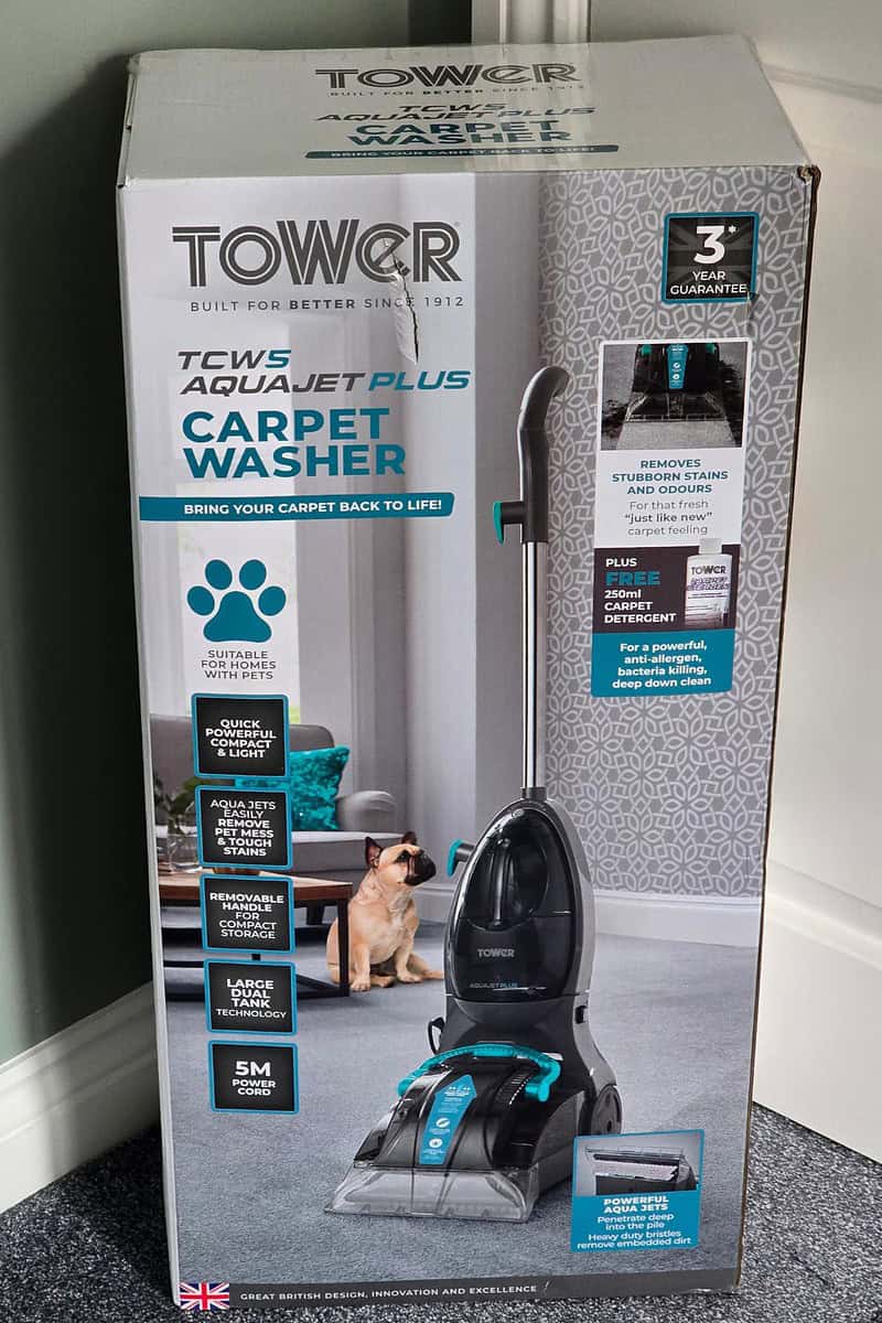 The box packaging of Tower's AquaJetPlus carpet washer highlights its impressive features, including pet stain removal, a 5m power cord, and a three-year guarantee. An image of a dog playfully lounging on the carpet is also included, setting the scene for your next glowing review.