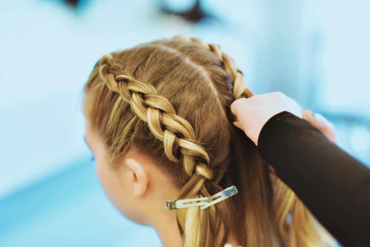 A person having their hair braided, with visible hair clips securing sections, showcases a trendy hairstyle that's perfect for the fitness lover on the move.