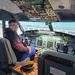 A person seated in a Flight Simulator cockpit at the FlightSimCentre, wearing a black and red long-sleeve shirt. The cockpit is filled with various controls and displays, capturing every detail of the immersive experience. An airplane with the word "Ryanair" is visible outside the window.