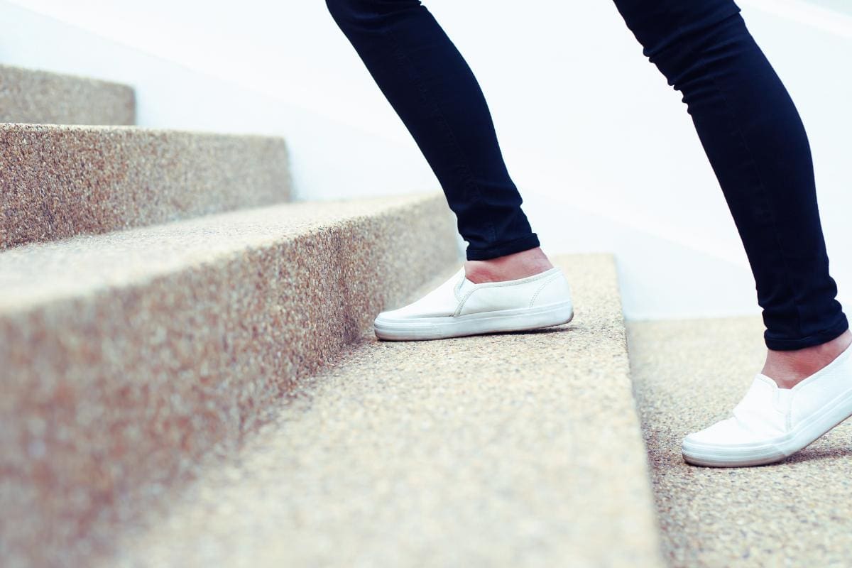 A woman's legs climbing the stairs doing no equipment exercises in leggings and comfy shoes.