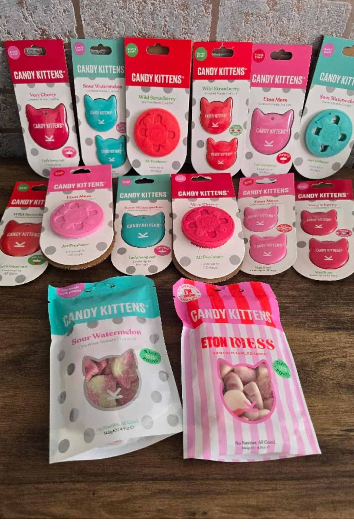 A display of Candy Kittens sweets and air fresheners in various flavors, like Wild Strawberry and Sour Watermelon—perfect road trip essentials for your next European road trip—arranged on a wooden surface against a tile background.