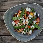 A vibrant summer barley grain bowl with snap peas, cherry tomatoes, sweetcorn, crumbled cheese, chopped nuts, and fresh herbs on a rustic wooden table—perfect for better health.
