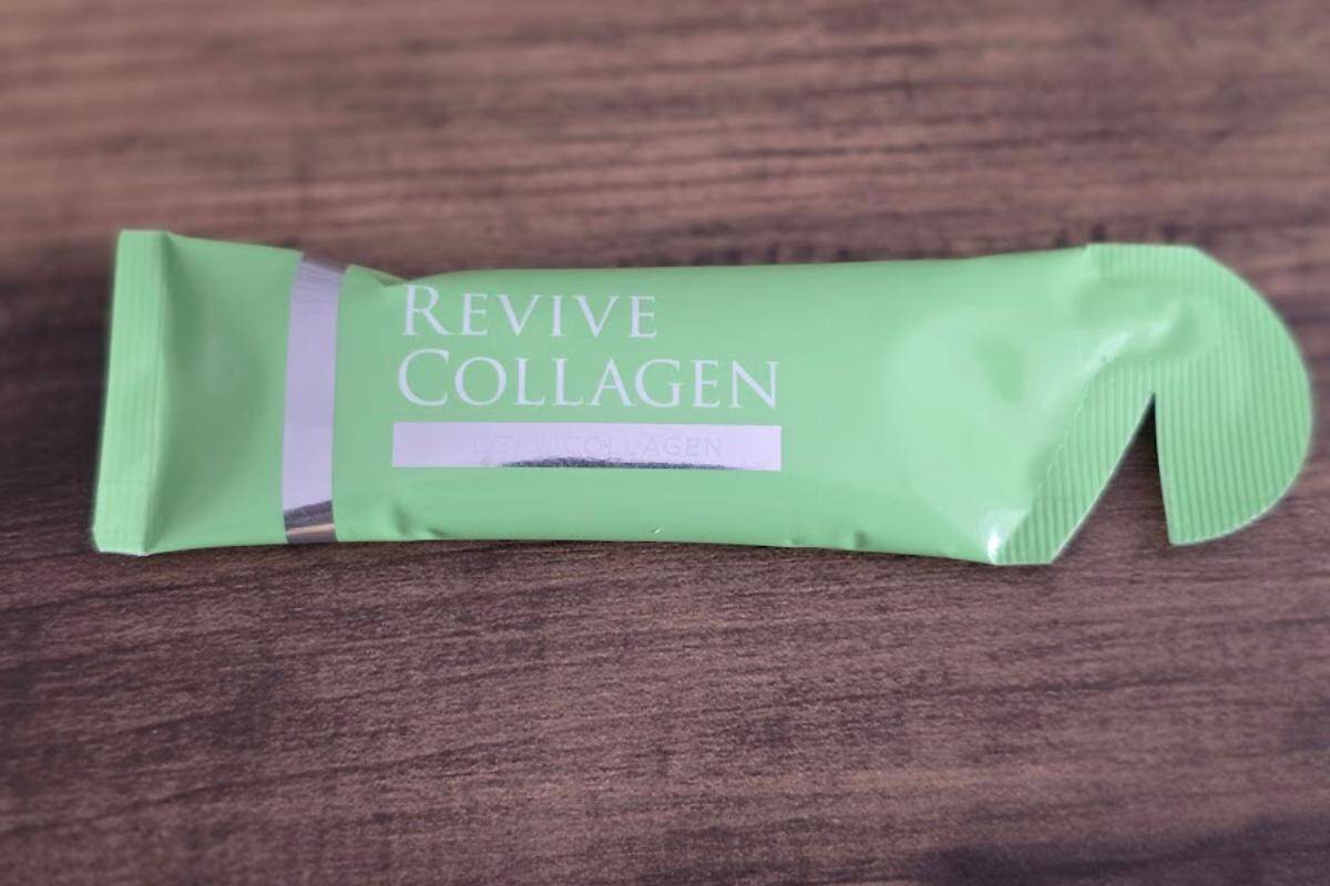 A green packet labeled "Revive Collagen" lies on a wooden surface. The partially opened packet, featuring silver accents, highlights Revive Collagen’s commitment to plant-based beauty with its vegan-friendly formula.