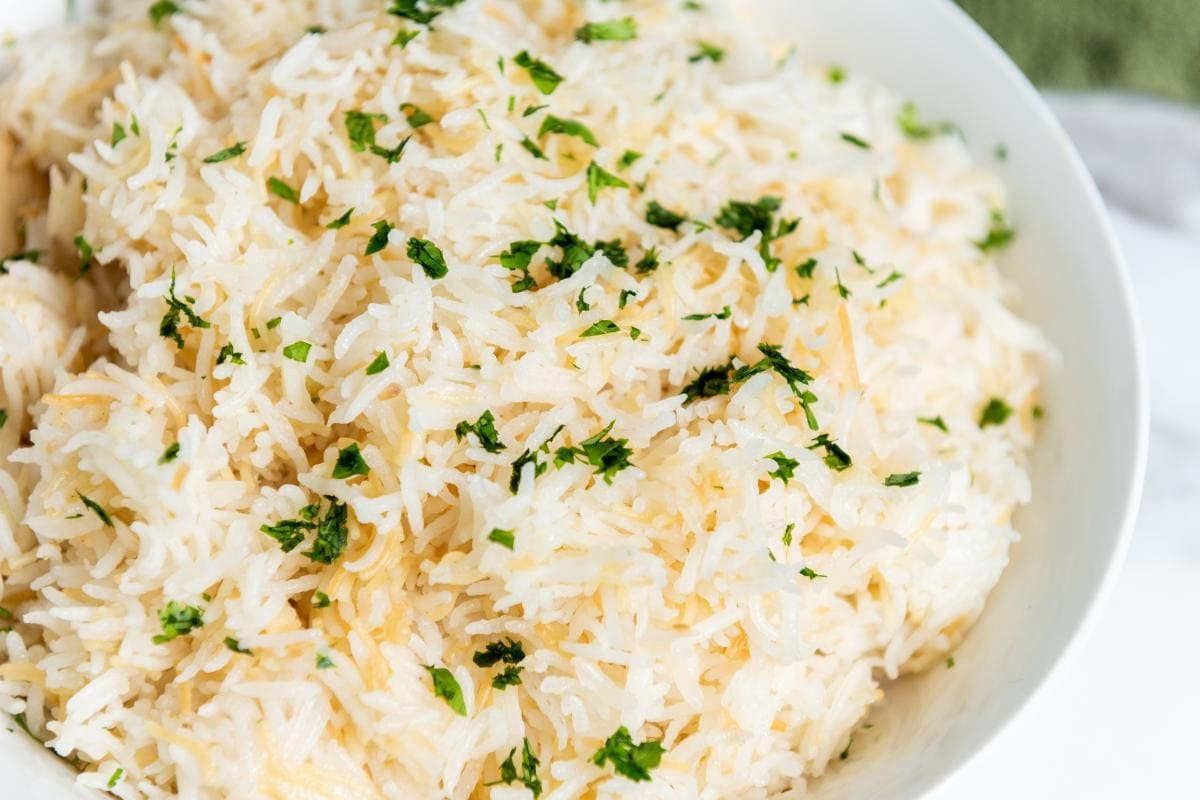 A close-up of a white bowl filled with fluffy, delicious rice, garnished with finely chopped fresh herbs—an easy side dish perfect for any meal.