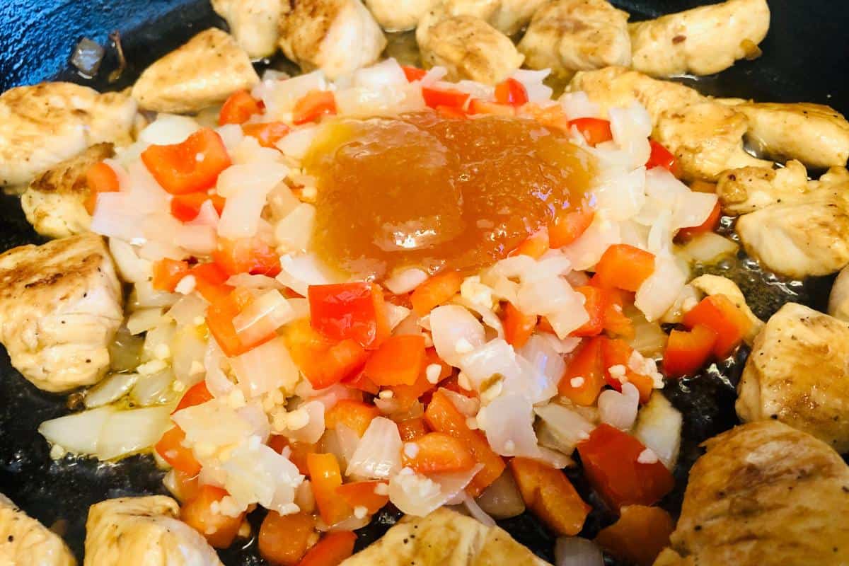 Diced chicken pieces surround sautéed onions and red bell peppers in a skillet, with a dollop of sauce or jelly placed in the center—perfect for topping your Healthy Chipotle Chicken pasta.