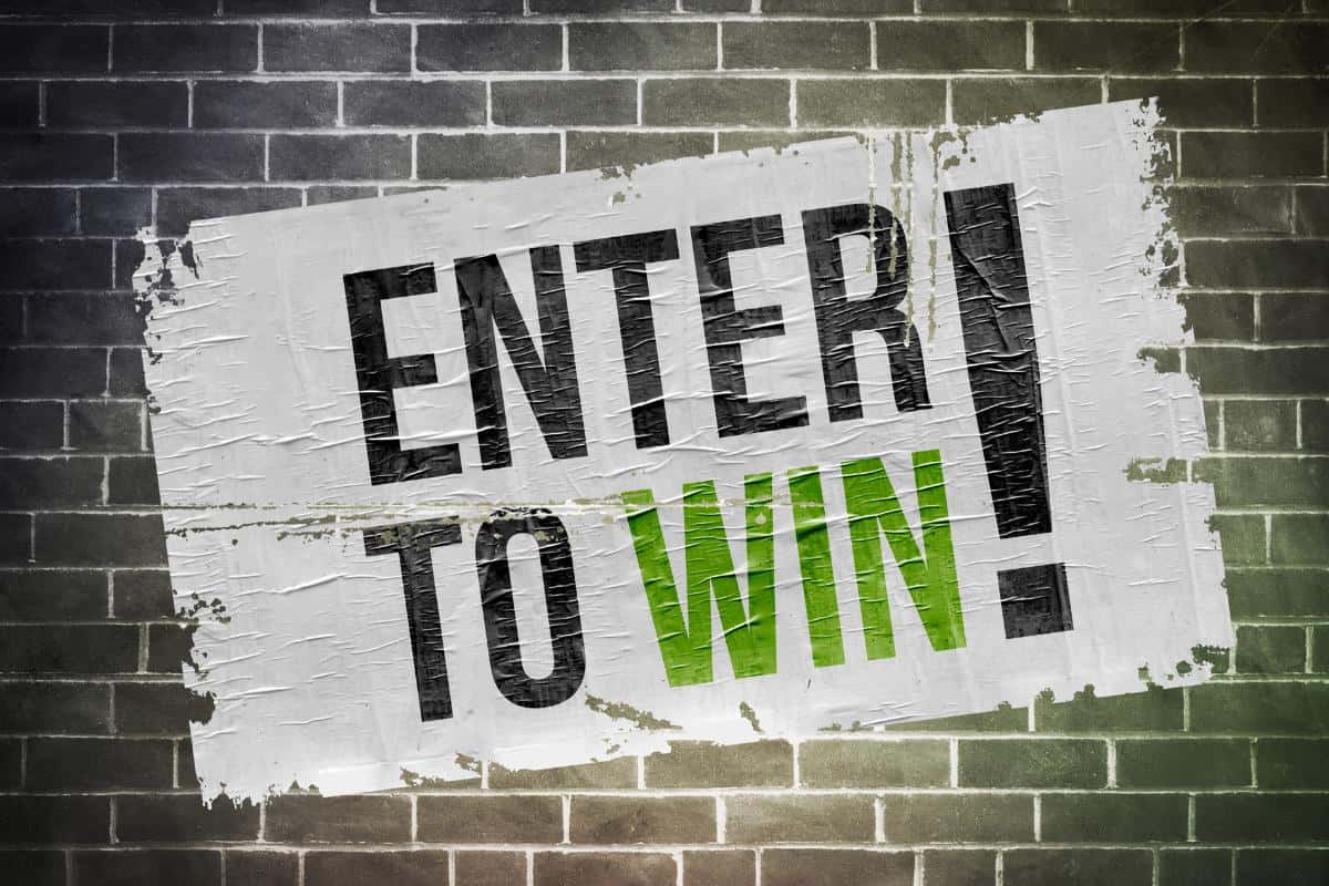 A textured white poster on a brick wall displays the bold words "ENTER TO WIN!" with "WIN £15 Amazon Voucher" highlighted in green.