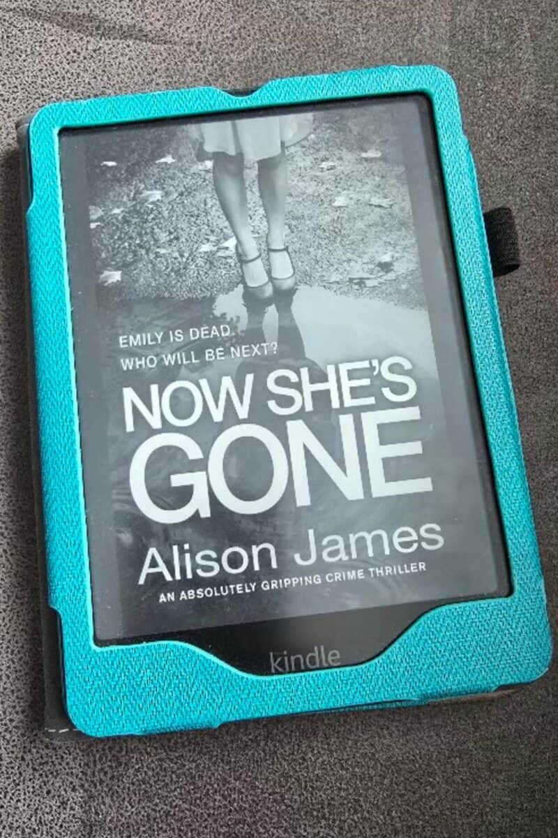 A Kindle e-reader in a turquoise case displays the cover of "Now She’s Gone" by Alison James, perfect for a Midweek Catch-Up, featuring a black-and-white image of a girl in a dress standing on a path.