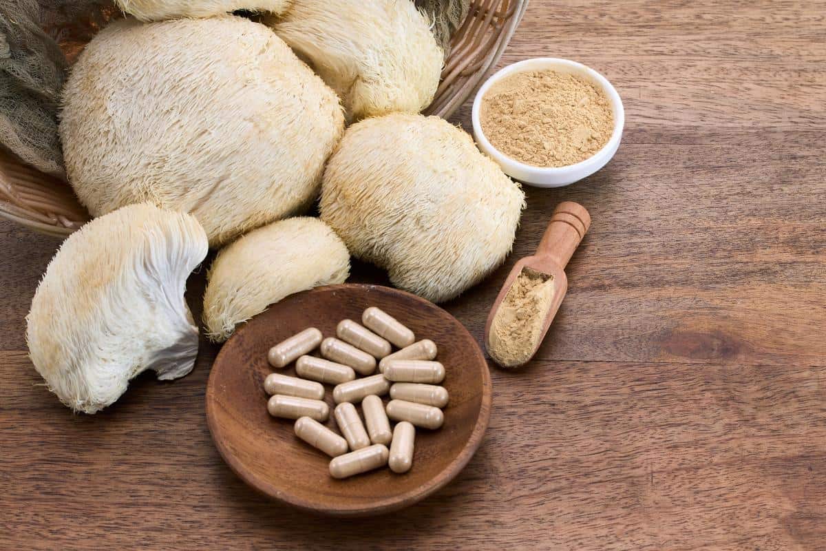 Lion’s Mane mushrooms on a wooden surface alongside a bowl of capsules, a small bowl of powdered weight loss supplement, and a wooden scoop with powder.