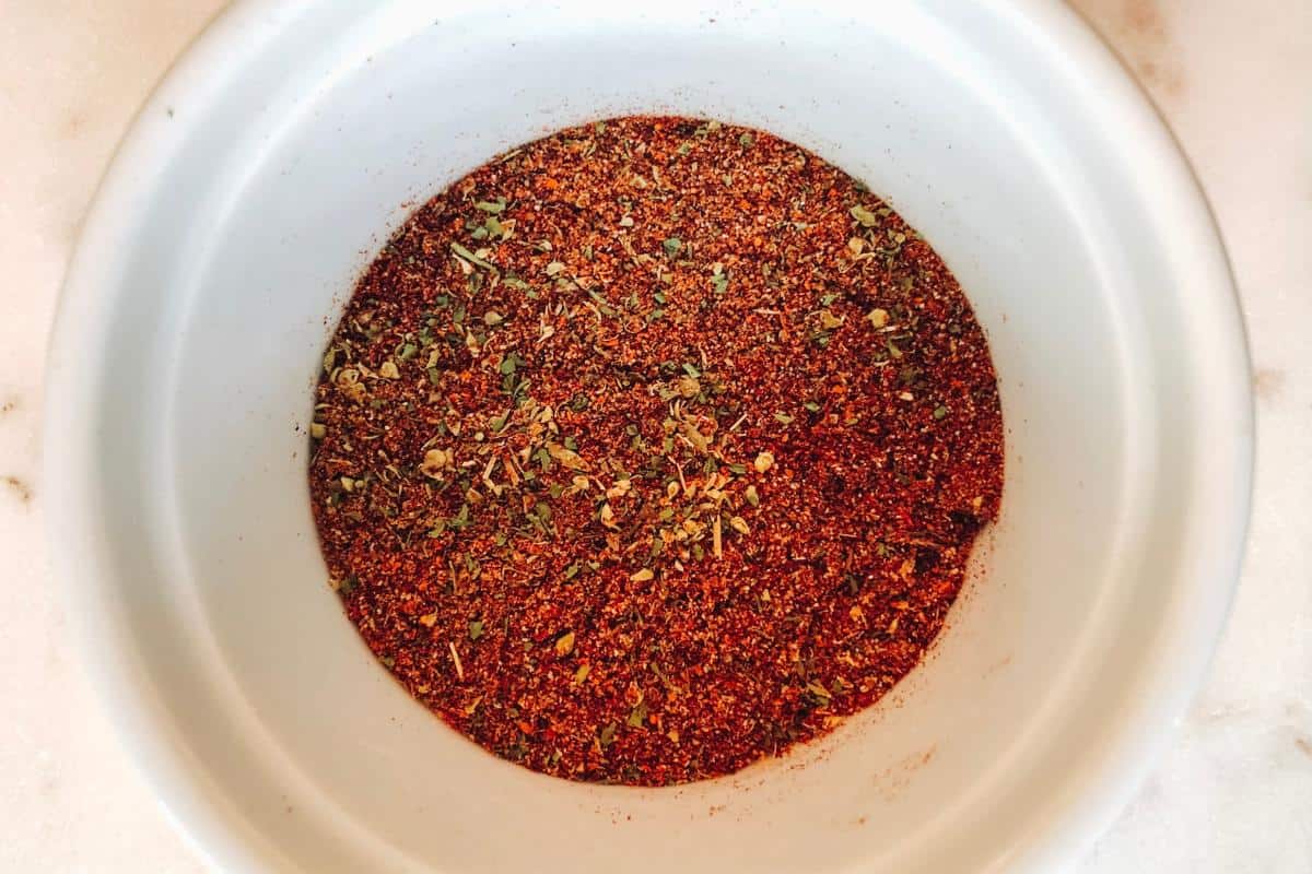 A white bowl filled with a reddish-brown spice mix, speckled with green dried herbs, sits on a light-colored surface—a perfect blend for an Easy Enchilada Recipe.