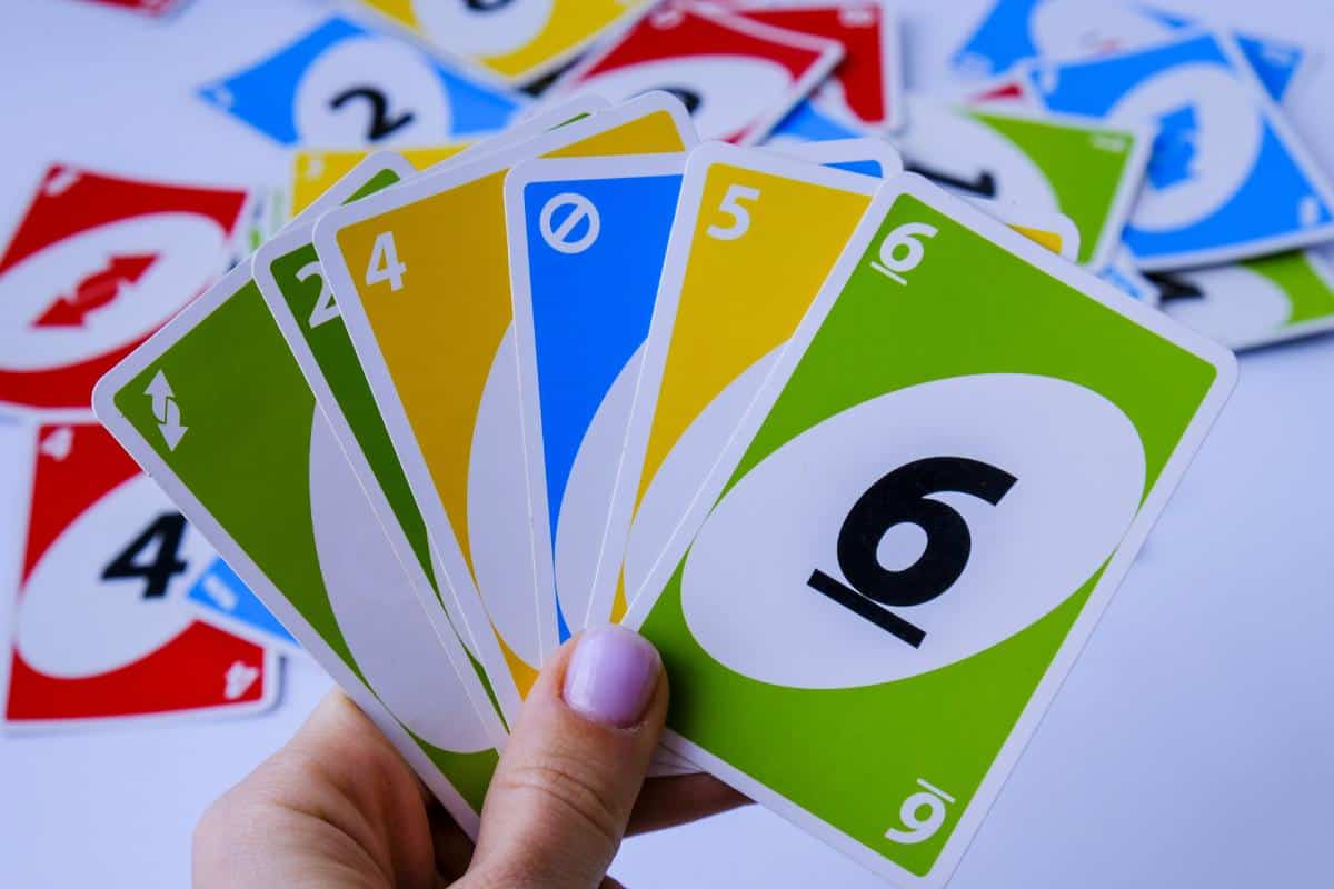 A hand holding five UNO cards—green reverse, yellow 4, blue skip, yellow 5, and green 6—against a scattered background of colorful UNO cards, perfect for family holiday games or lightweight family games together.