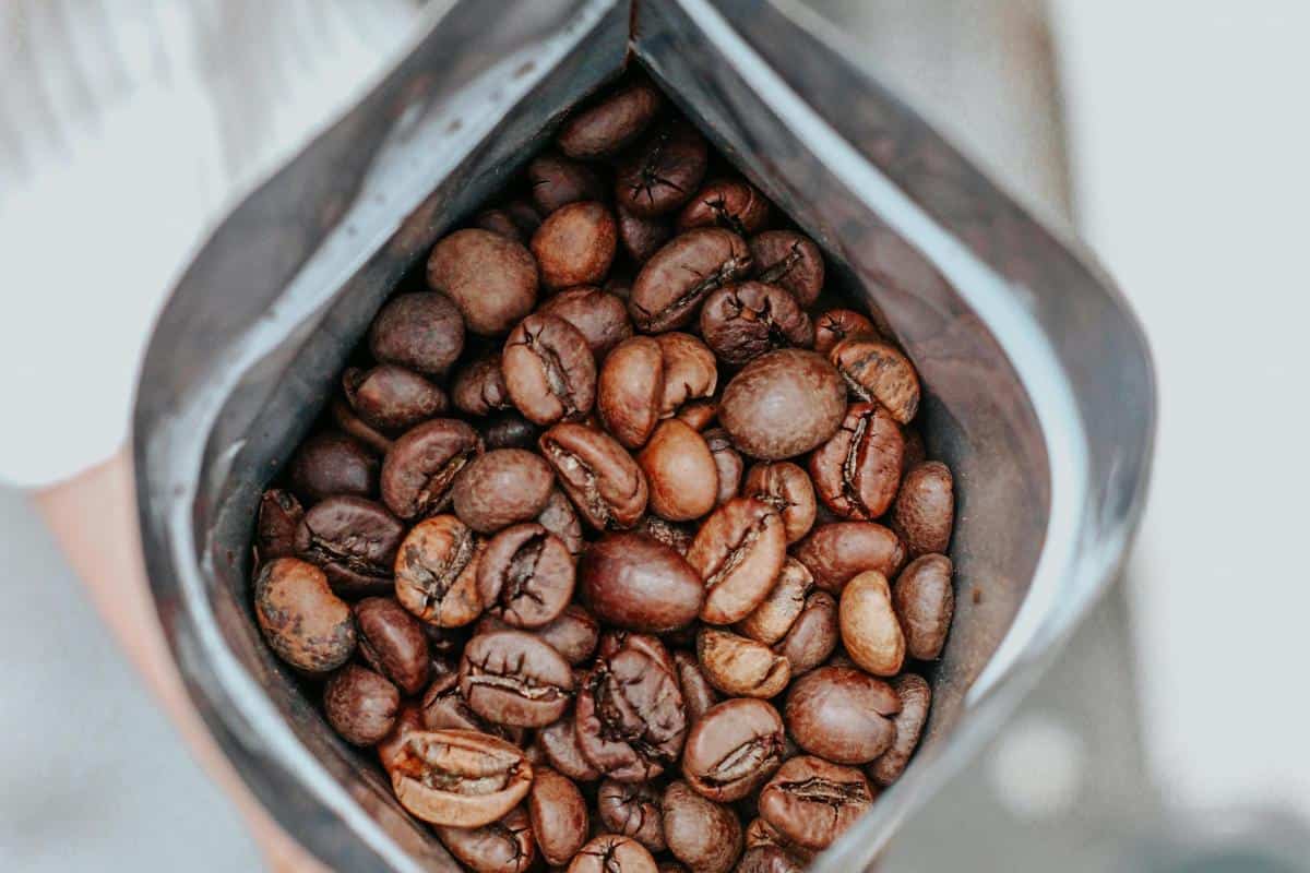 An open bag filled with whole roasted coffee beans, viewed from above, shows glossy brown beans inside a silver-lined package—perfect for those who enjoy the aroma of freshly ground beans.