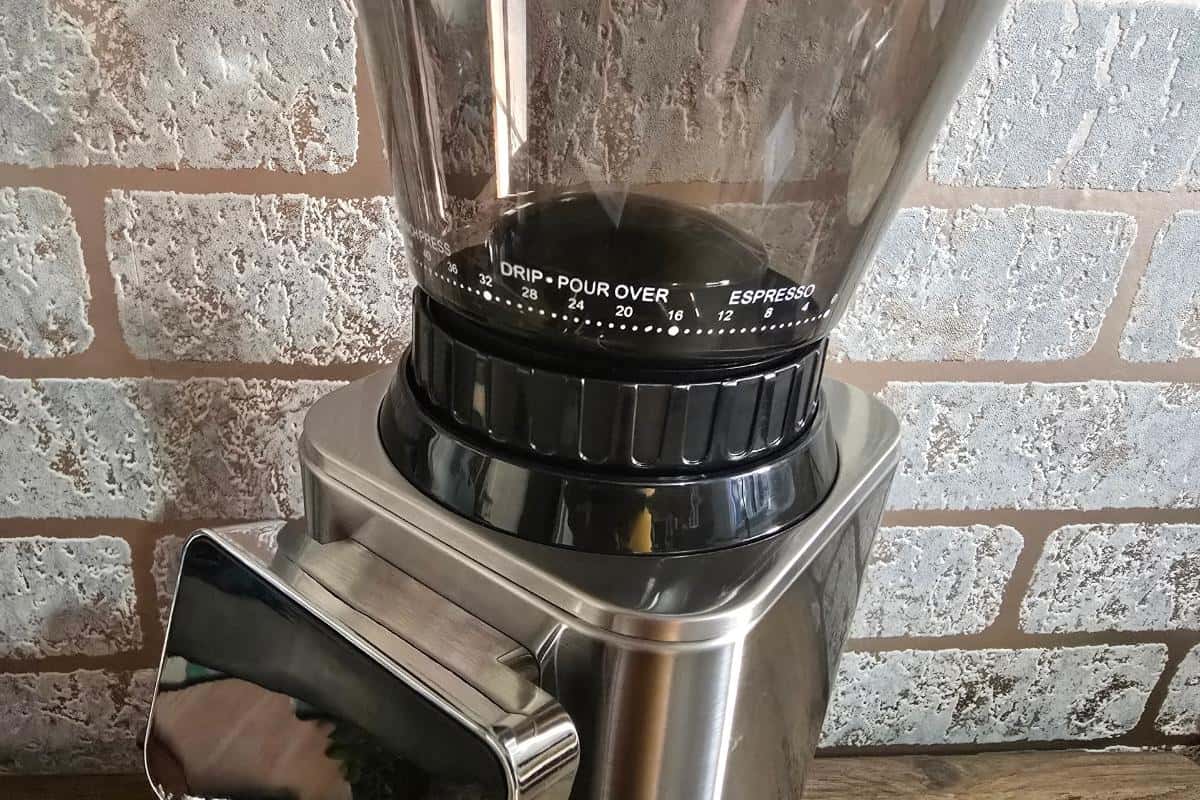 A close-up of a coffee grinder on a countertop, showing the grind size selector for drip, pour-over, and espresso, perfect for enjoying freshly ground beans against a brick wall background.