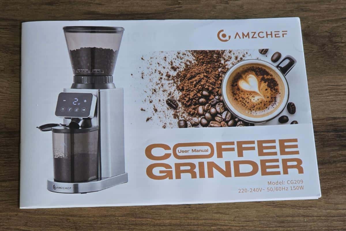 AMZCHEF coffee grinder user manual on a wooden surface, featuring a photo of the grinder, freshly ground beans, a cup of latte with heart art, and product details including model CG209 and 150W power.