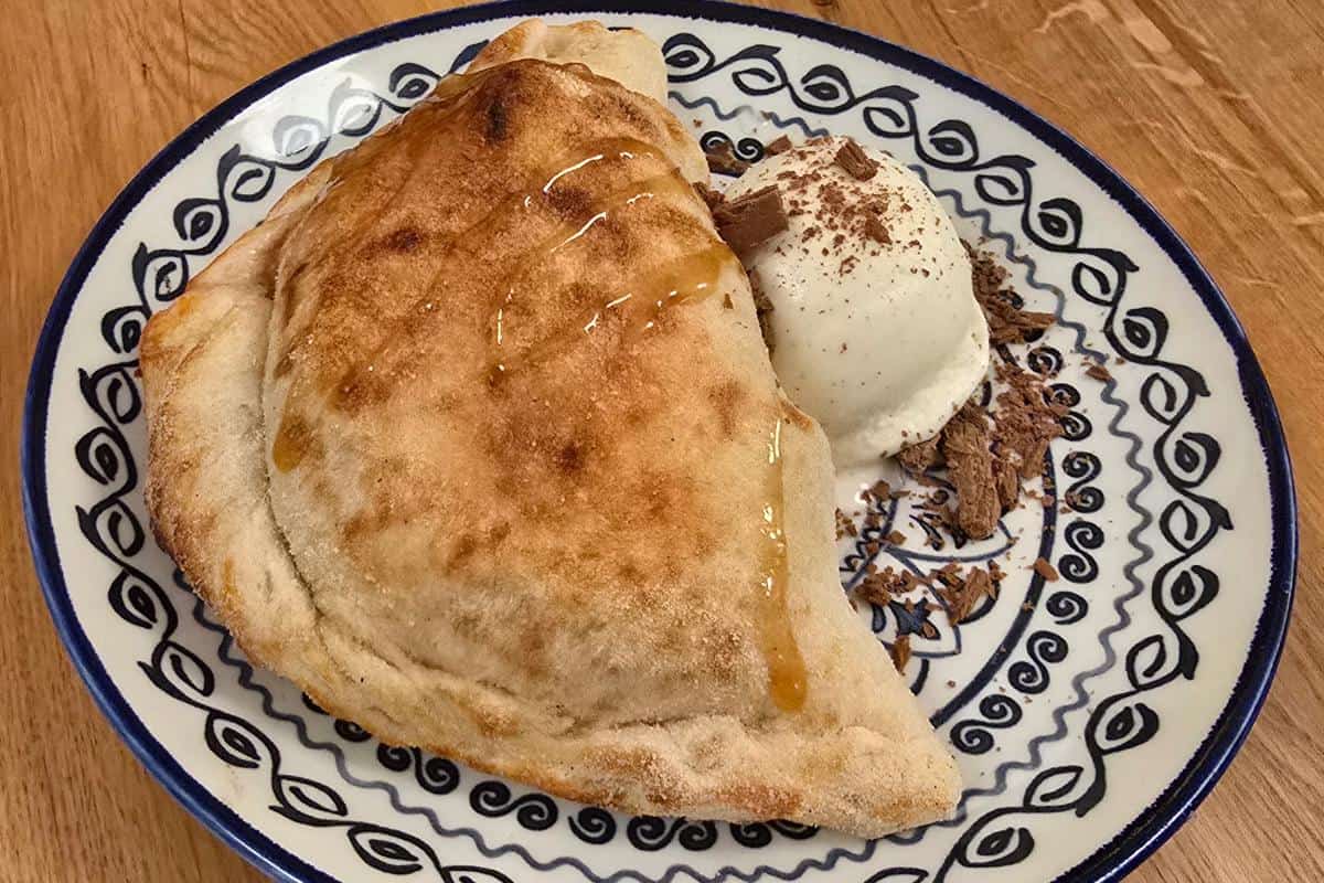 A calzone drizzled with honey is served on a patterned plate alongside a scoop of vanilla ice cream sprinkled with cinnamon and chocolate shavings—an indulgent treat you might find at Prezzo Italian Nottingham.