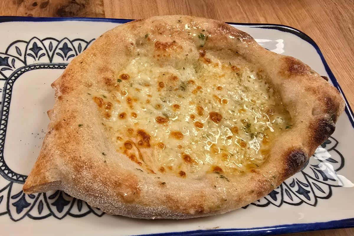 A cheesy pide, a Turkish flatbread with melted cheese and a golden, bubbly crust, is served on a decorative white and blue plate on a wooden table—perfect for your next review after dining at Prezzo Italian Nottingham.