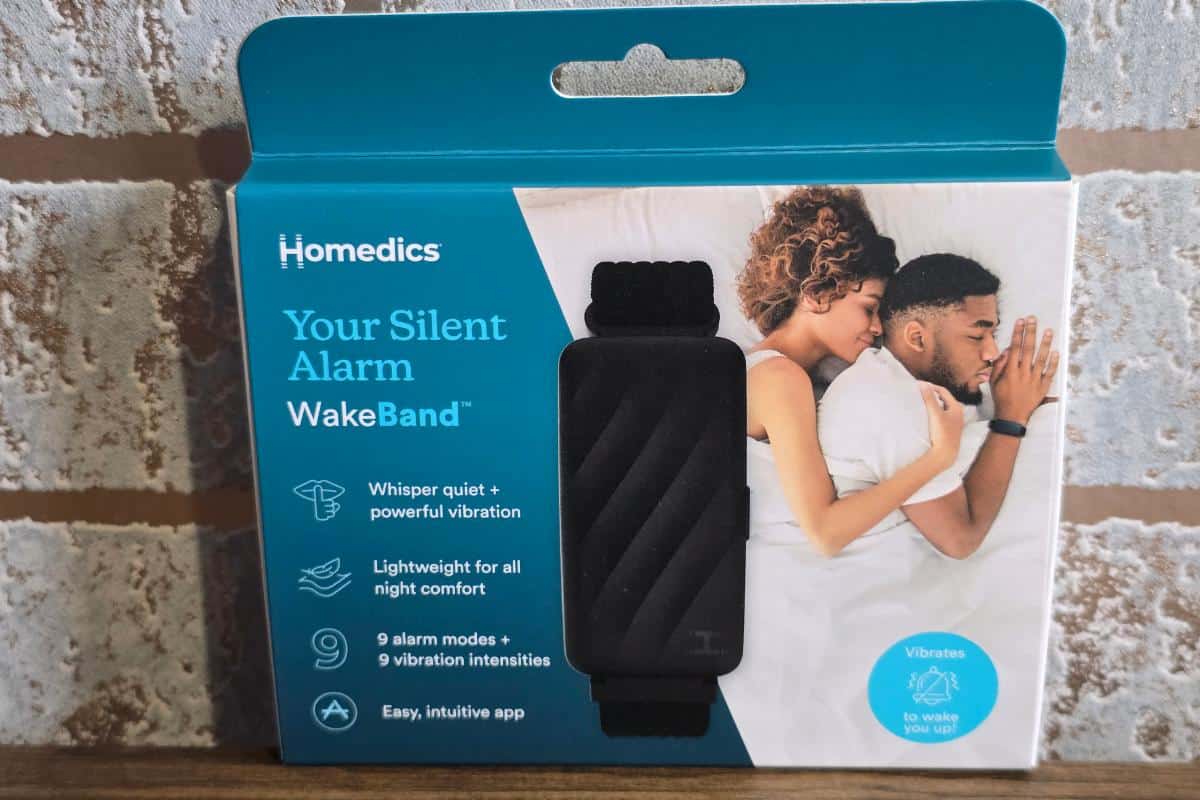A product box for the HoMedics WakeBand shows a black wristband in the center, with an image of a couple sleeping. The package highlights features like "whisper quiet," "powerful vibration," nine alarm modes, and its silent alarm function.