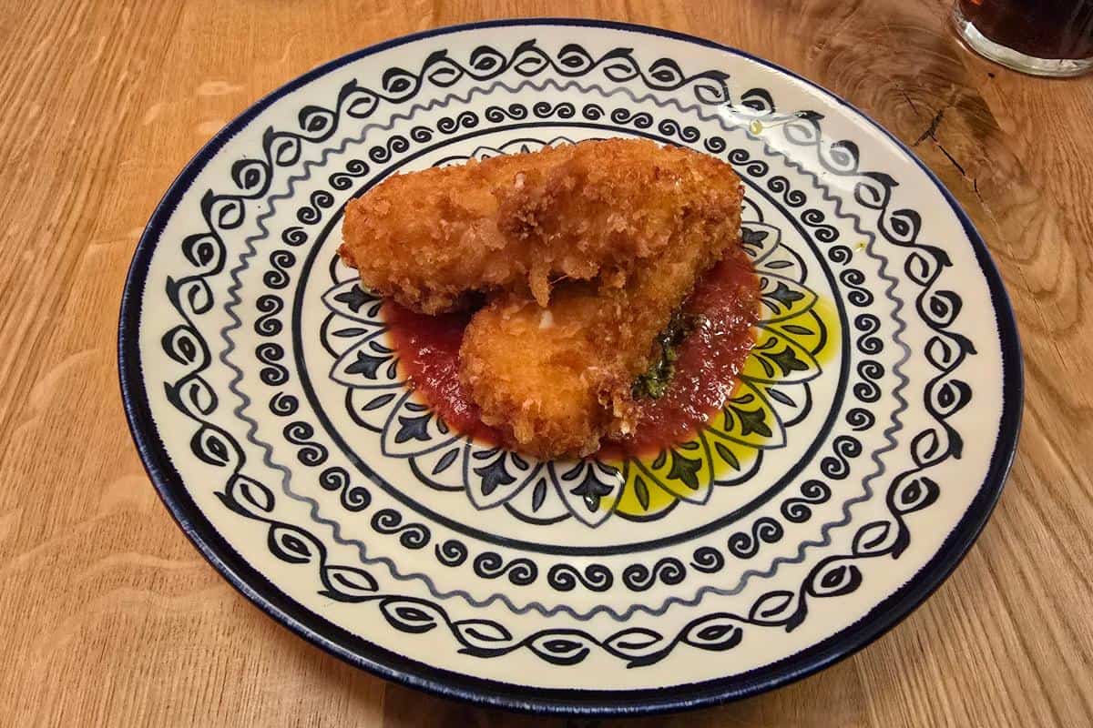 Two pieces of golden-brown fried food served on a decorative plate with a red sauce underneath, placed on a wooden table at Prezzo Italian Nottingham.