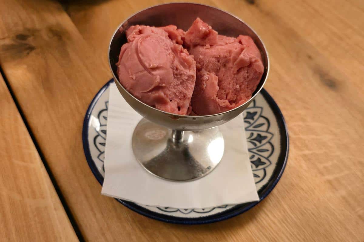 A metal dessert cup filled with three scoops of pink sorbet sits on a white napkin and patterned plate atop a wooden table at Prezzo Italian Nottingham.
