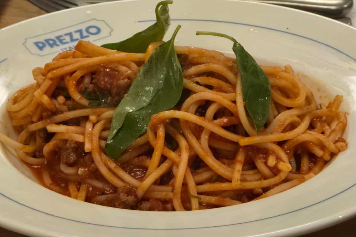 A plate of spaghetti with meat sauce, topped with fresh basil, served in a white dish marked "Prezzo"—perfect for a restaurant review of Prezzo Italian Nottingham. Forks are visible in the background.