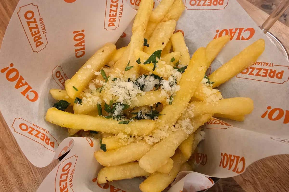 A serving of golden French fries topped with grated cheese and herbs, placed in a paper-lined basket branded with “PREZZO ITALIAN” and “CIAO!”—a delicious bite perfect for your next Nottingham Prezzo Italian review.