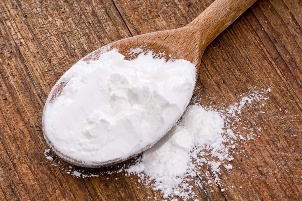 A wooden spoon holds a heap of white powder, with some spilled onto a rustic wooden surface—perfect for those seeking healthy cornflour alternatives to thicken sauces.