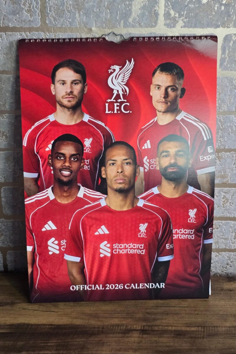 A 2026 official calendar featuring five male Liverpool FC players in red jerseys posing before a vivid backdrop—perfect for Gifts for Him or as a top pick in your Christmas Gift Guide. Displayed against a light-colored brick wall.