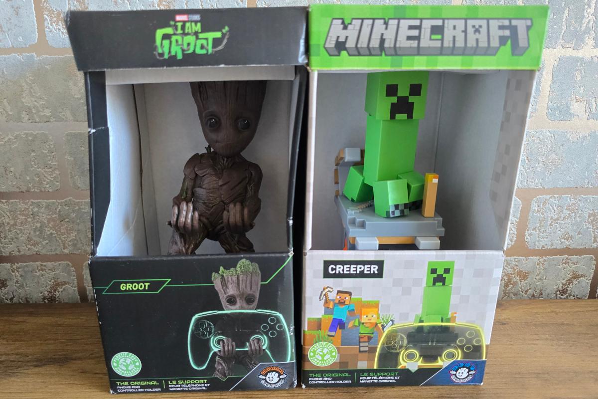 Two boxed figurine holders on a wooden surface—one of Groot from "I Am Groot," and one of a green Creeper from "Minecraft"—make perfect gifts for him and are a fun addition to any Christmas Gift Guide, both designed to hold game controllers.