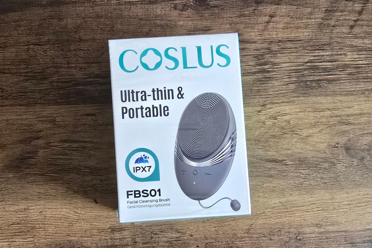 A box of a COSLUS ultra-thin and portable facial cleansing brush (model FBS01) featuring IPX7 waterproof rating on a wooden surface—perfect for any Christmas Gifts for Her. The box shows an image of the device and product details.