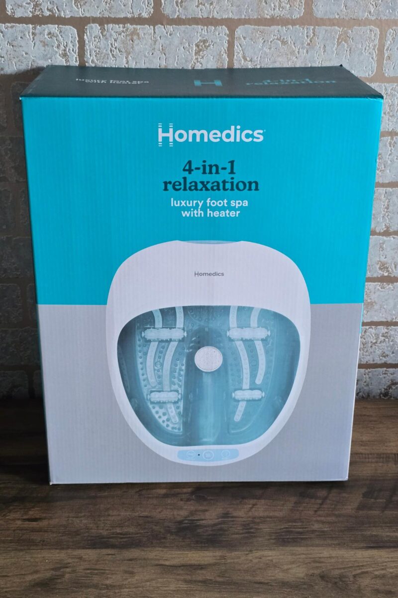 A boxed Homedics 4-in-1 relaxation luxury foot spa with heater, perfect for Christmas presents, featuring an image of the product on the blue and white packaging, set against a brick wall background.