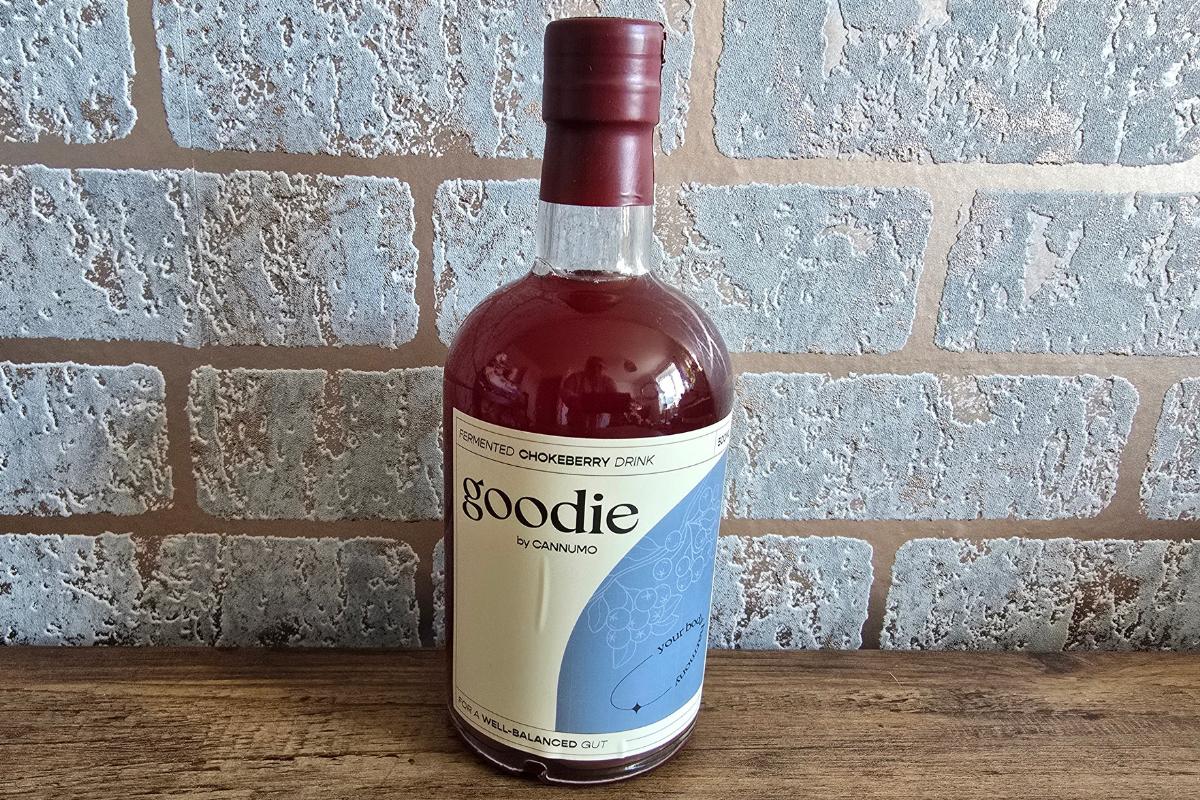 A bottle of Goodie sweetened chokeberry drink with a maroon cap and white label, placed on a wooden surface in front of a brick-patterned wall—perfect as a Secret Santa surprise or Stocking Filler.