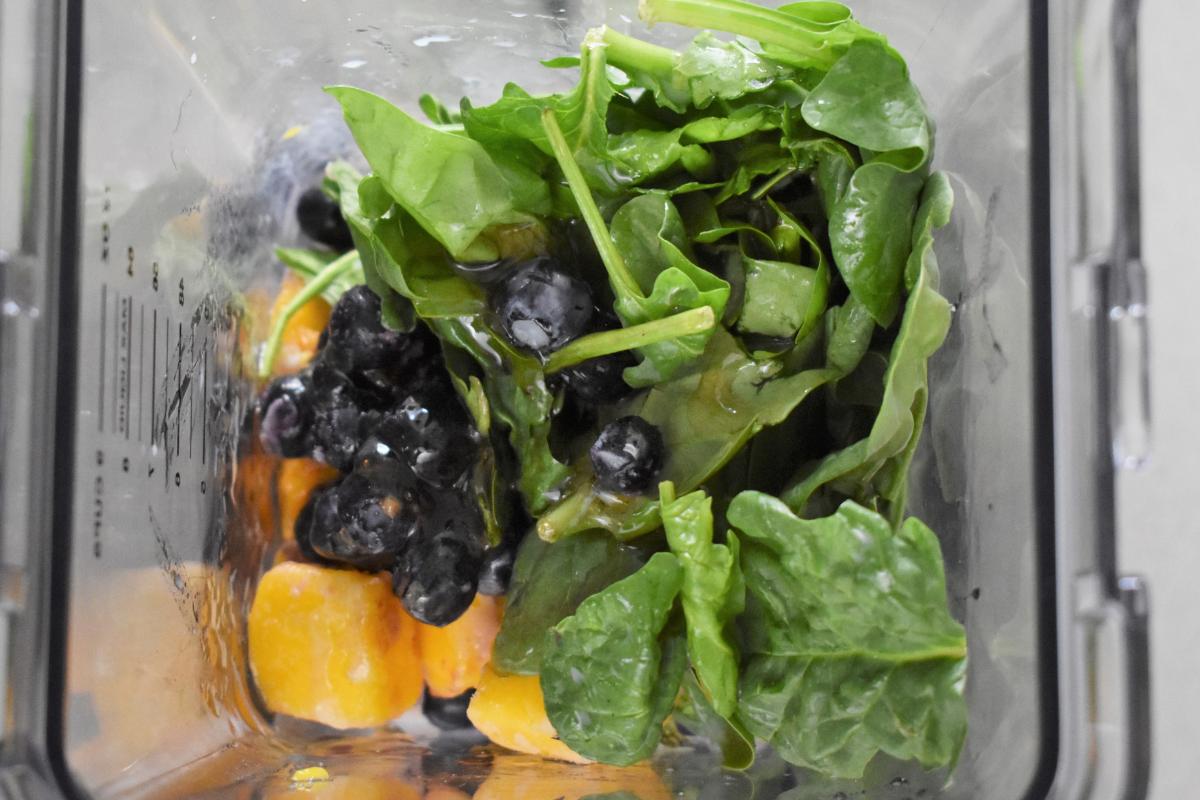 Fresh spinach leaves, juicy blueberries, and orange frozen fruit chunks sit in a blender, ready to be transformed into a delicious smoothie recipe.
