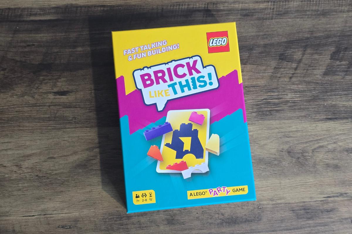 A colorful LEGO party game box titled "Brick Like This!" sits on a wooden surface. With its bright yellow, blue, and purple design, it's a standout choice for any children's gift guide, featuring LEGO bricks and a puzzle piece on the front.