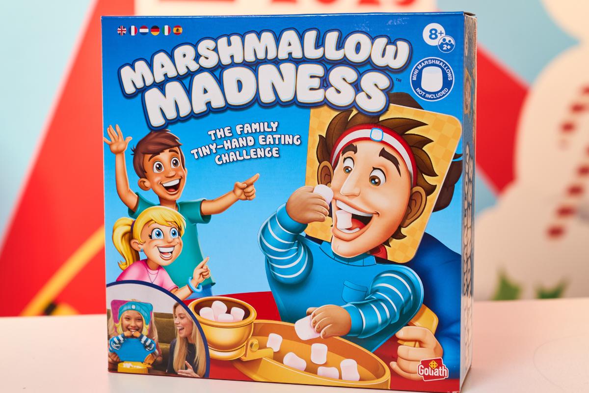 The image shows "Marshmallow Madness: The Family Tiny-Hand Eating Challenge" by Goliath, a Top Toys 2025 pick. The box features cartoon kids using small hands to eat marshmallows—perfect for any Christmas list and recommended for ages 8 and up.