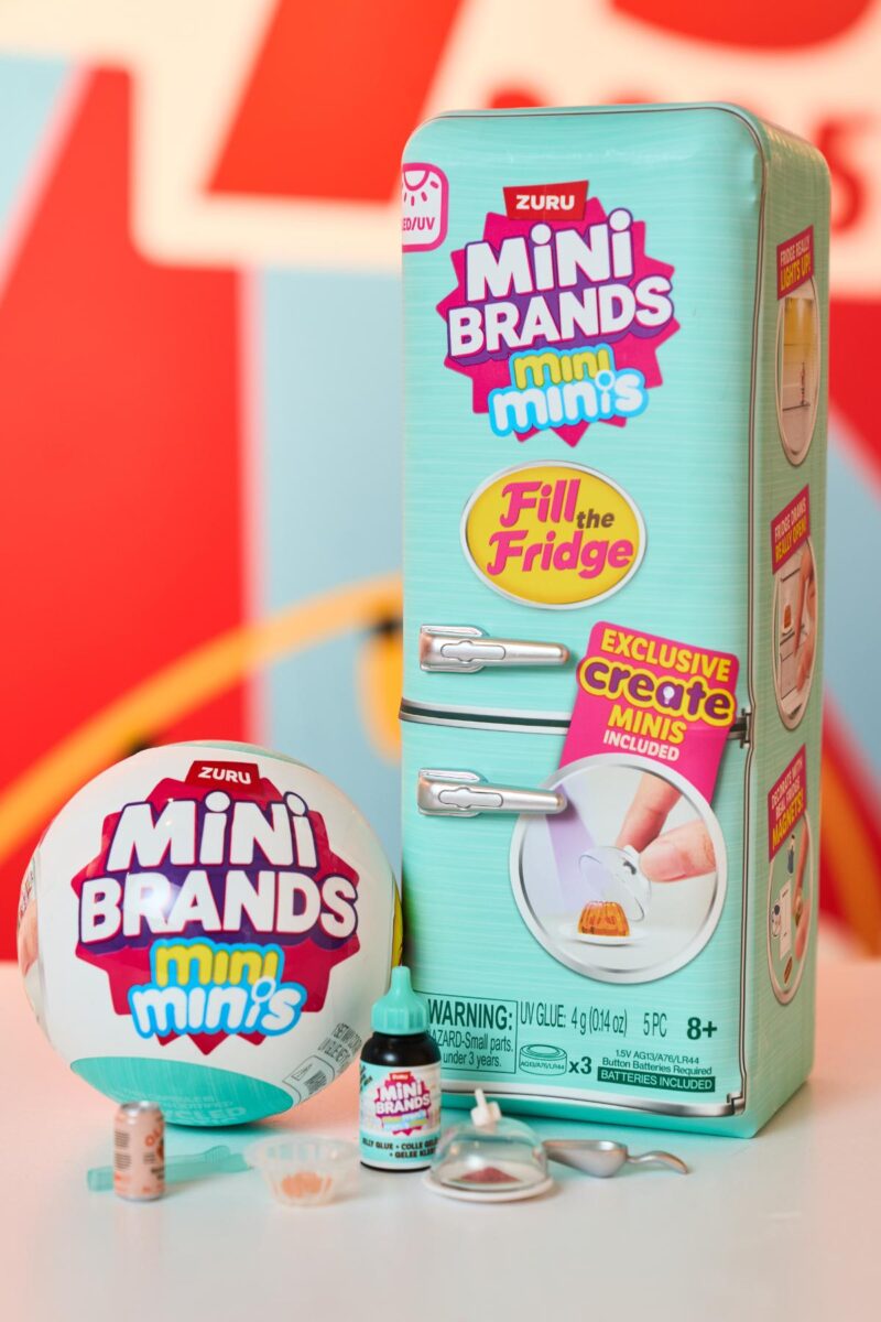 A ZURU Mini Brands Mini Minis toy set—perfect for kids’ Christmas lists and sure to be one of the top toys of 2025—features a fridge-shaped box, round ball container, and miniature food items against a colorful, blurred background.