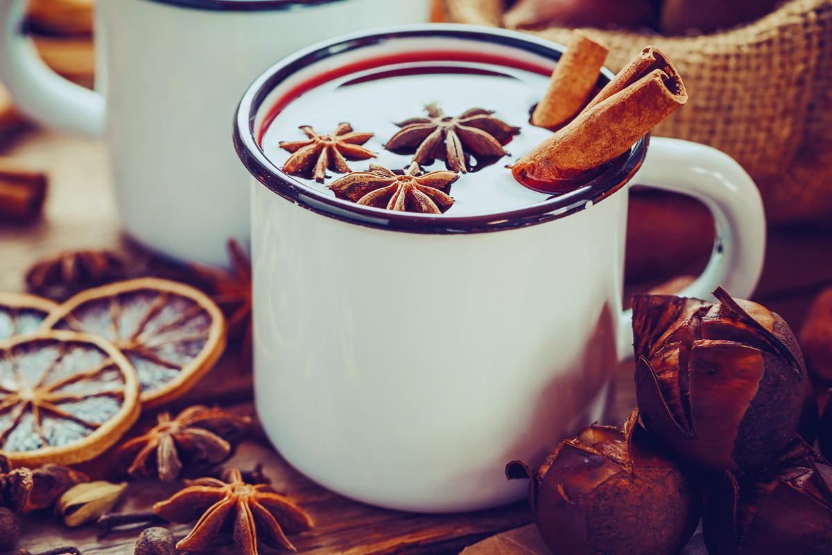 A white enamel mug filled with a spiced drink, garnished with star anise and cinnamon sticks. Dried citrus slices and extra spices rest nearby, evoking the warmth of a healthier mulled wine perfect for cosy evenings.