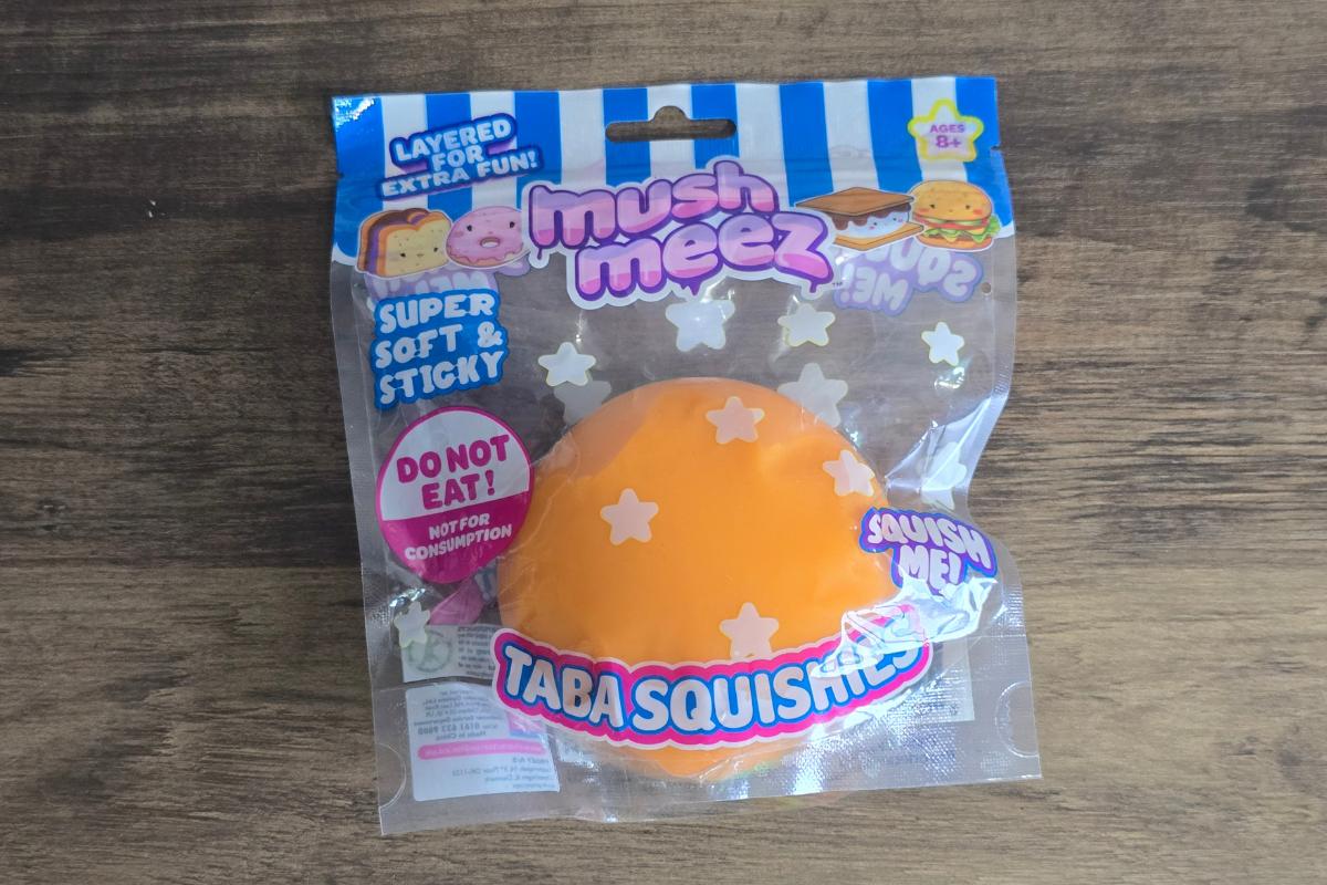 A packaged orange squishy toy with white stars, labeled "Mush Meez Taba Squishies." Featured in many children's gift guides, the packaging warns "Do not eat! Not for consumption" and advertises the toy as super soft and sticky.