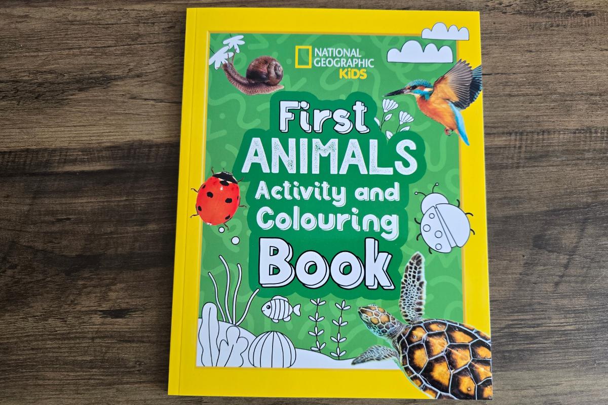 A "National Geographic Kids First Animals Activity and Colouring Book" with a yellow border, green background, and animal illustrations sits on a wooden surface—a perfect pick for any children's Christmas gifts or featured in a children's gift guide.