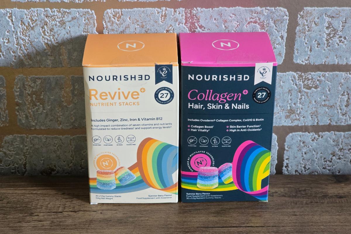 Two boxes of Nourished gummy supplements sit on a wooden surface against a brick wall—a perfect addition to your Christmas Gift Guide for Her. The Revive box is orange, whilst Collagen+ Hair, Skin & Nails comes in pink.