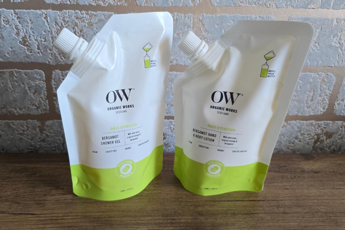 Two white and green OW Organic Works refill pouches—Bergamot Shower Gel and Hand & Body Lotion—sit on a wooden surface. Perfect as a Stocking Filler or for your Gift Guide, these daily essentials hydrate with fresh, uplifting scent.