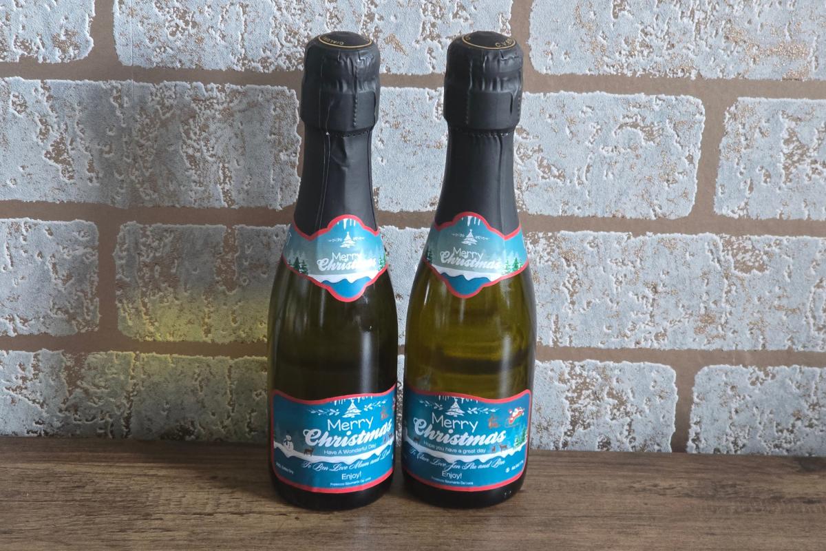 Two bottles of sparkling wine with festive "Merry Christmas" labels stand side by side on a wooden surface—perfect as a Stocking Filler or Secret Santa surprise in your holiday Gift Guide.