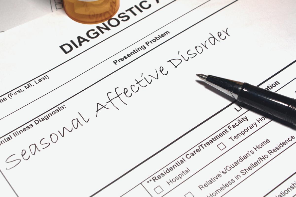 A medical form labeled "Diagnostic" with "Seasonal Affective Disorder (SAD)" handwritten under “Presenting Problem.” A black pen and part of a pill bottle are visible, highlighting the impact of winter depression.