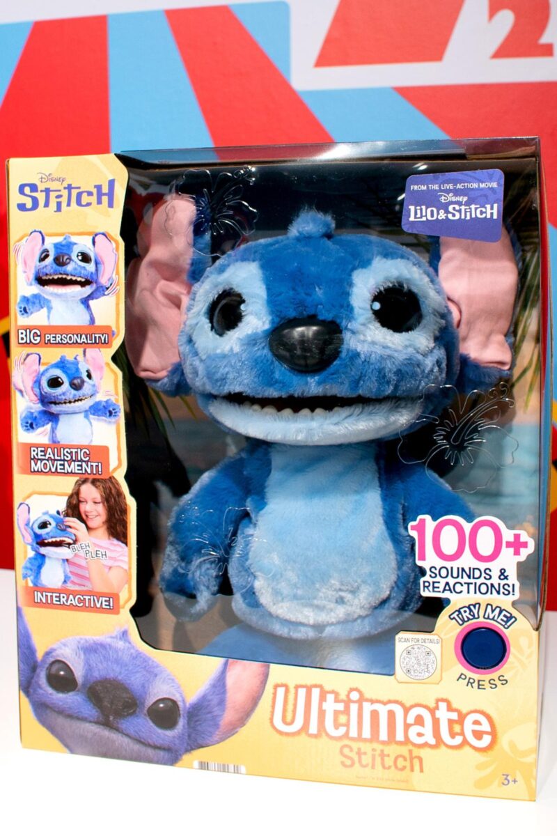 A plush toy of Stitch from Disney's "Lilo & Stitch" is displayed in a colorful box, making the Top Toys 2025 Christmas List for kids with its 100+ sounds, realistic movement, and interactive features. The packaging features movie images.