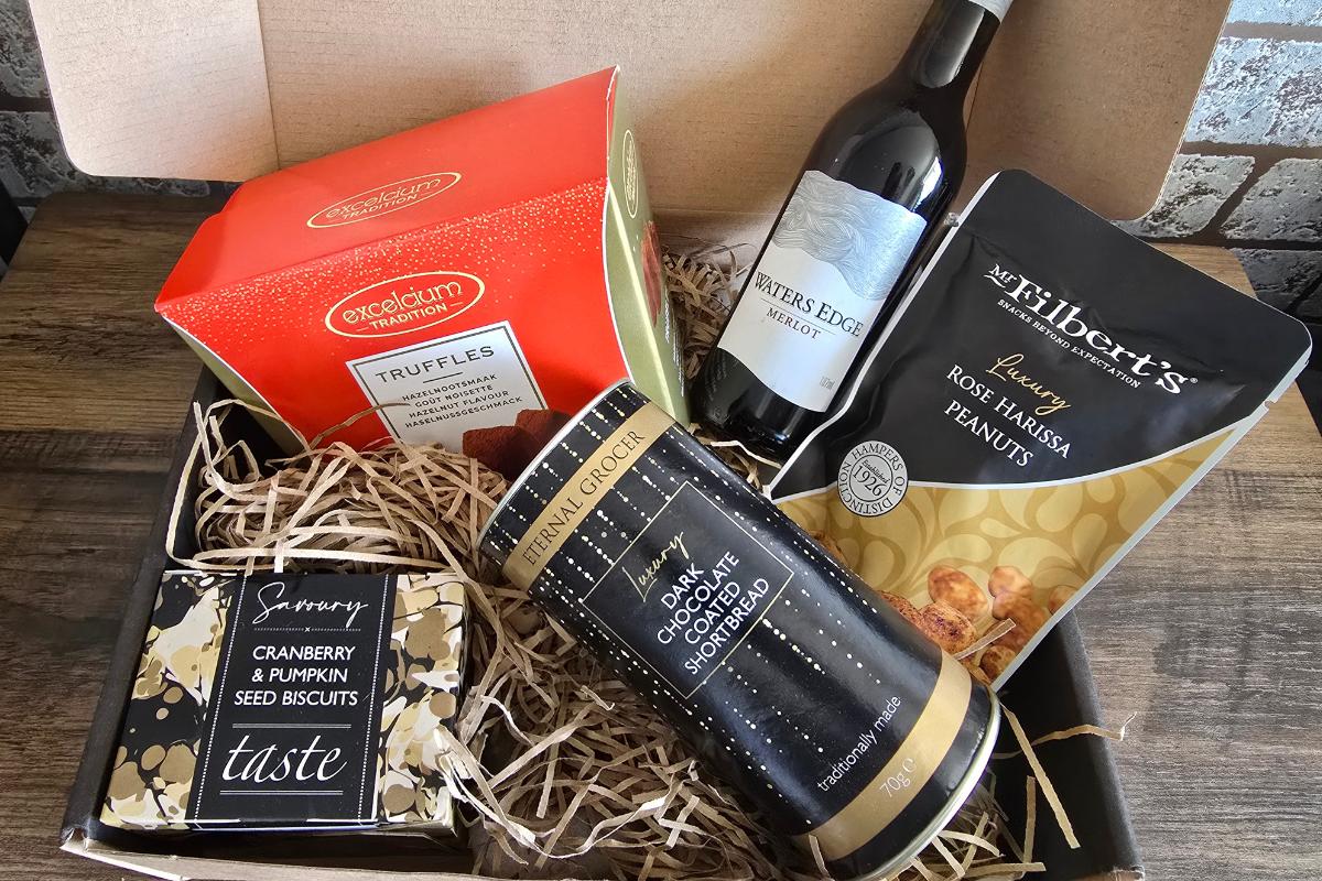 A gift box filled with cranberry & pumpkin seed biscuits, dark chocolate & orange shortbread, rose harissa peanuts, truffles, and red wine—perfect for any Gift Guide for Families and festive celebrations.