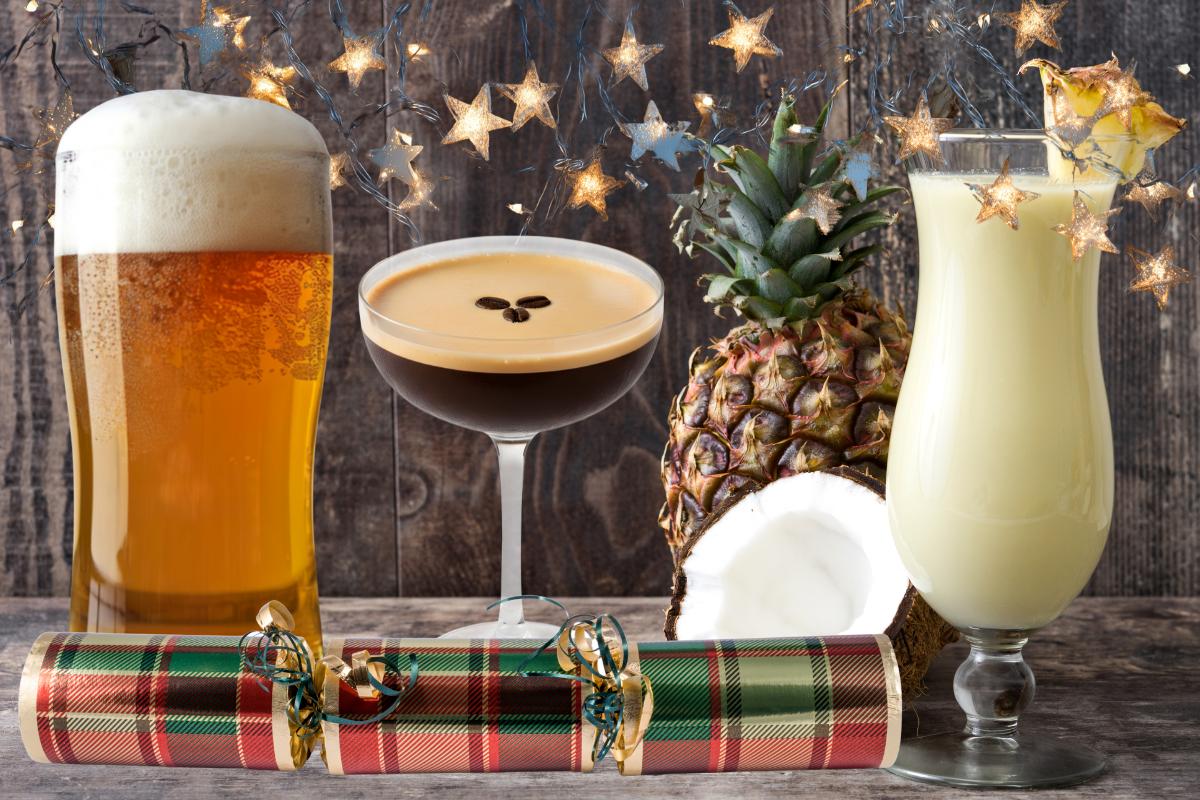 A pint of beer, an espresso martini, a piña colada, a whole pineapple, a halved coconut, a Christmas cracker, and star-shaped fairy lights create festive vibes, unhealthy drinks to avoid if you’re focused on weight loss this Christmas and New Year.