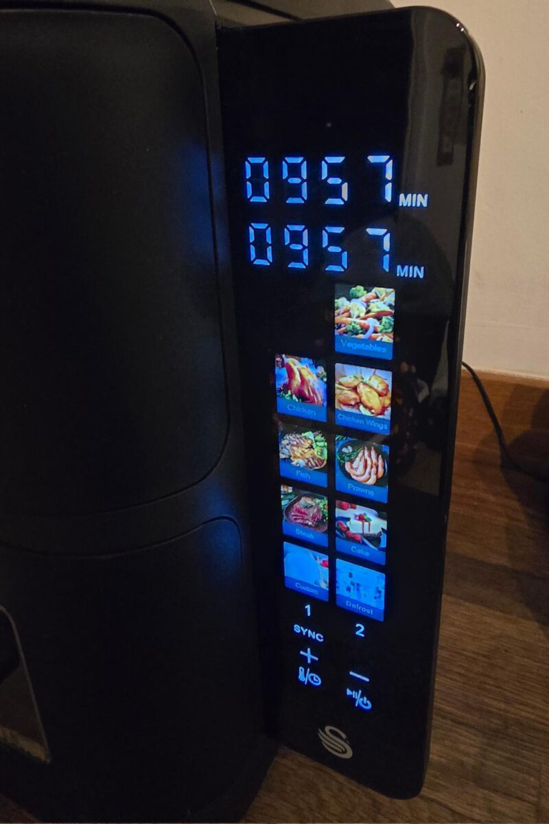Close-up of a glossy, modern Swan 11L Duo Layer Air Fryer display, showing a timer set to 9:57 and illuminated icons for chips, chicken, fish, bacon, and more cooking options.